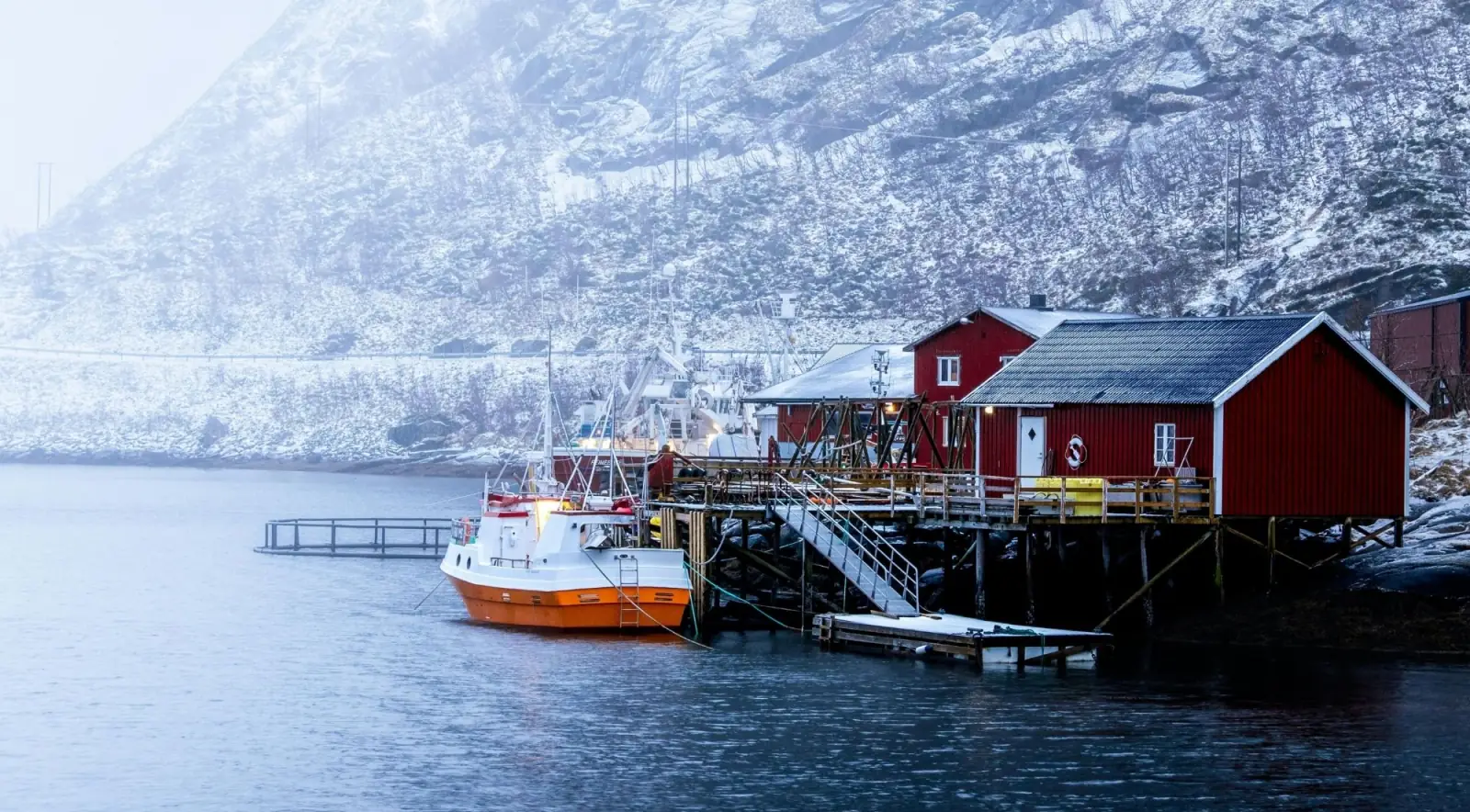 Traditional red rorbu cabins and a small boat at a snowy waterside